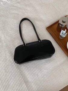 Detailed close-up view of a sleek black leather shoulder bag on a textured white fabric surface.
