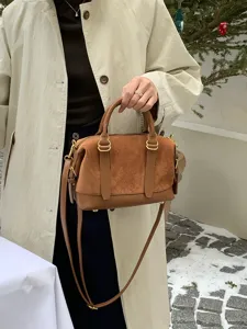 Close-up display of retro brown suede bowling handbag featuring golden hardware and practical strap.