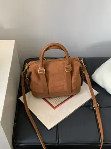 Detail view of a retro brown suede bowling handbag with metal hardware and dual top handles.