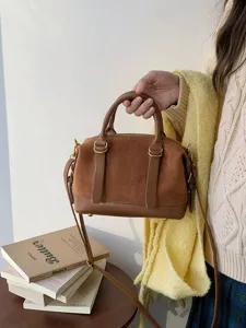 Detailed view of retro brown suede bowling bag with shoulder strap and metal hardware details.