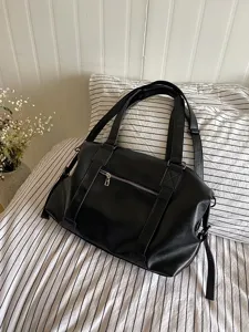 Detail view of black leather travel bag, casual bedroom setting with striped bedding.