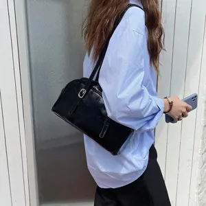 Black glossy leather underarm shoulder bag detail shot showing smooth texture and metal buckle.
