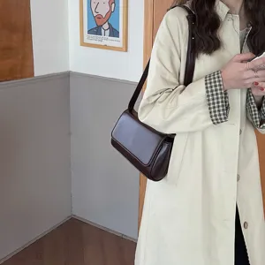 Λεπτομερής λήψη vintage σκούρας καφέ δερμάτινης τσάντας ώμου με μπεζ καμπαρντίνα.
