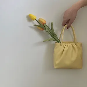 Detailed view of a trendy yellow pleated square mini handbag featuring double top handles.