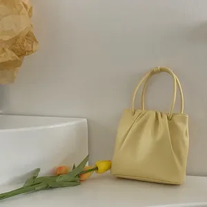 Detailed view of a light yellow pleated mini handbag featuring dual top handles and cute design.