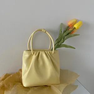 Yellow pleated handbag detail view, elegant minimalist design with top handles and tulip decor.