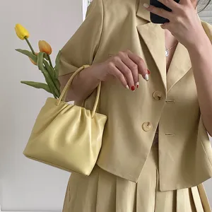 Close-up detail of the pastel yellow pleated handbag paired with matching outfit and tulips.