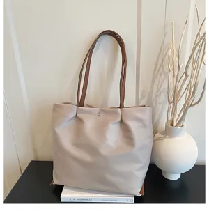 Close-up detail of the light grey oxford cloth tote bag with brown straps on clean tabletop.