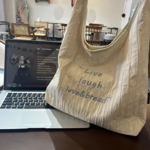 Detailed view of casual beige canvas tote bag with letter embroidery for daily commute.