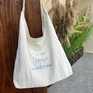 Detail shot of the cream white canvas tote bag featuring stylish blue embroidered lettering.