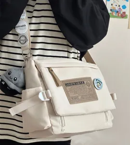 Detailed shot of a casual beige canvas messenger bag worn across the body, featuring retro badge.