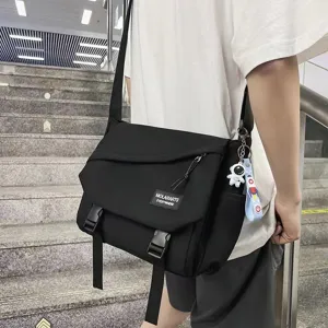 Detail view of stylish black canvas messenger bag with astronaut keychain for daily commute.