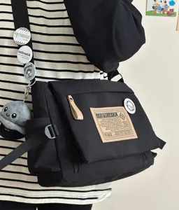 Detail shot of black canvas messenger bag with cool badges and plush keychain, casual daily wear.