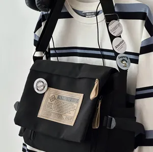Detailed view of the black canvas messenger bag showing front woven label and custom badges.