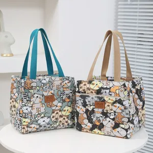 Canvas lunch bag with cute cat print, dual handles, and front pocket shown on a white table.