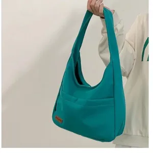 Detail view of a teal canvas shoulder bag featuring a convenient front pocket and leather label.