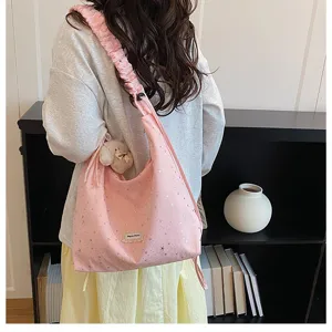 Detail view of a pink slouchy tote bag with star prints, ruffled strap, and a cute bear pendant.