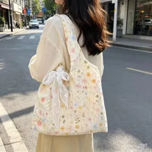 Detail shot of floral embroidered canvas tote bag with white lace bow on shoulder.