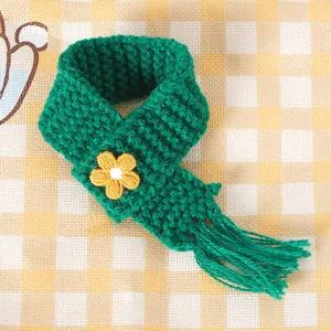 Mini groene gebreide poppensjaal met gele bloemborduursel, perfect als schattig accessoire.