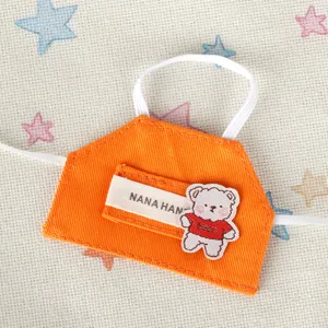 Dettaglio della mini bavetta per bambola 10cm, tessuto arancione con patch orsetto.