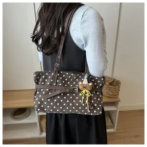 Dettaglio borsa shopper a pois marrone con design di cintura e ciondolo orsetto nella stanza.