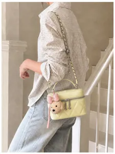 Detail shot of yellow quilted vanity bag with chain strap and cute bear charm in indoor scene.