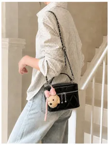 Detail shot of chic black quilted chain crossbody vanity bag with cute puppy plush charm.