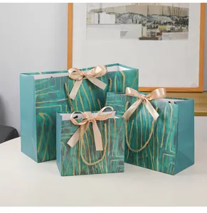 Groene papieren cadeautjes tassen met gouden accenten, satijnen strikken en elegant design.