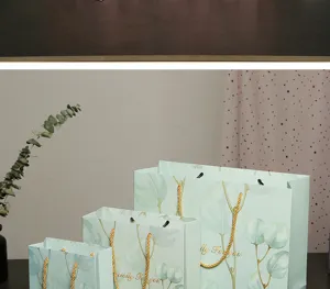 Sacchetti regalo in carta verde mint con stampa di foglie di eucalipto e manici dorati.