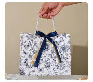 Blauw-witte vlinder papieren cadeauzak met elegante satijnen strik voor feestdagen en kledingverpakking.