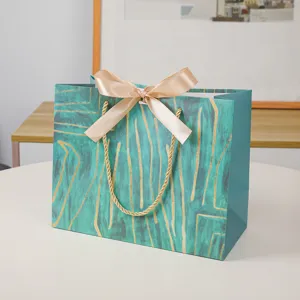 Groene papieren geschenkzak met gouden lijnen en strik voor winkelen en kleding.