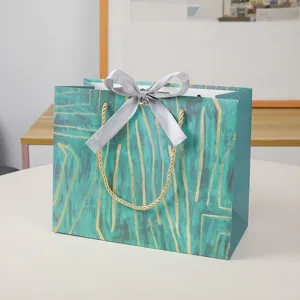 Groene papieren cadeautas met grijze strik en gouden lijnen, elegante verpakking voor kleding.