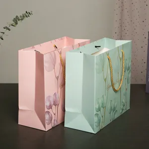 Sacchetti regalo in carta con foglie di eucalipto rosa e verde con manici dorati per feste.
