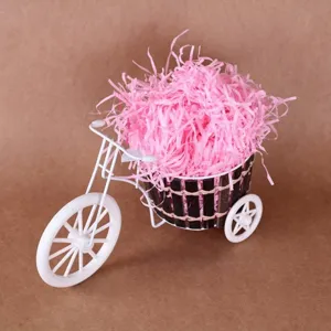 Roze rafia papier snippers als vulling voor geschenkdozen in een witte decoratieve fiets.
