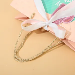 Grande sacchetto regalo in carta rosa con manici dorati e nastro bianco per compleanno.