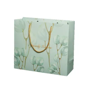 Elegante sacchetto regalo in carta verde chiaro con foglie di eucalipto e manici dorati.
