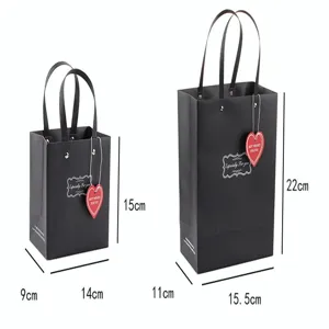 Bolsas de regalo de papel negro con asas y etiquetas de corazón en dos tamaños distintos.