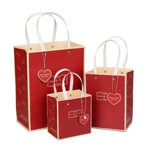 Juego de tres bolsas de regalo de papel rojo y crema con asas de cinta y etiquetas.