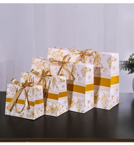 Gedetailleerd overzicht van witte papieren geschenkzakjes met gouden bloemenprint en strik.