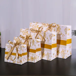 Elegante witte papieren geschenkzakjes met gouden bloemmotieven en linten voor verpakking.