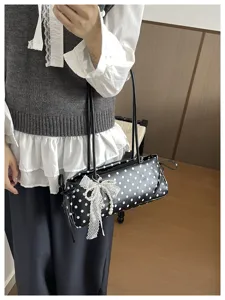 Primo piano e dettaglio della borsa a spalla a pois neri con fiocco in pizzo e perle.