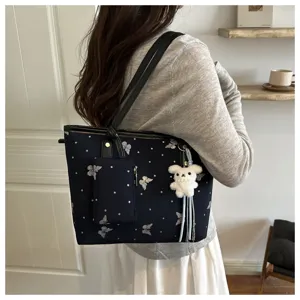 Detail view of dark blue tote bag with butterfly print, cute bear keychain and pouch.