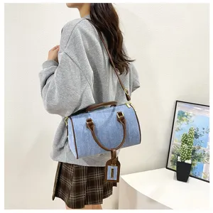 Casual denim Boston handbag detail shot, featuring brown leather handles and shoulder strap.
