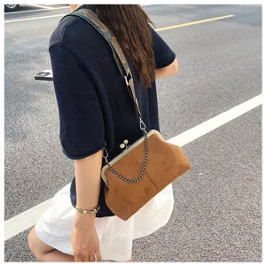 Detail shot of retro brown suede kiss-lock shoulder bag with wide strap and chic chain.
