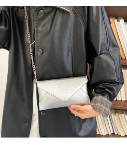 Detail shot of stylish silver envelope crossbody bag with gold chain strap and crinkled texture.