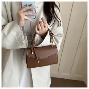 Stylish brown crossbody bag detail view featuring unique knot handle and chic envelope flap design.