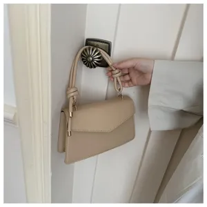 Minimalist beige shoulder bag detail view featuring elegant knotted handle and gold tone hardware.