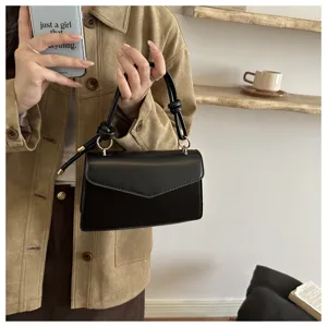 Fashionable minimalist black leather shoulder bag with stylish knotted top handle for women.