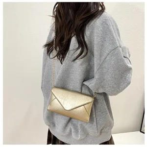 Close-up detail of the stylish gold envelope chain crossbody bag worn by the model indoors.