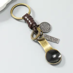 Vintage metalen lepel sleutelhanger met bruin leer gevlochten touw en decoratieve hangers.